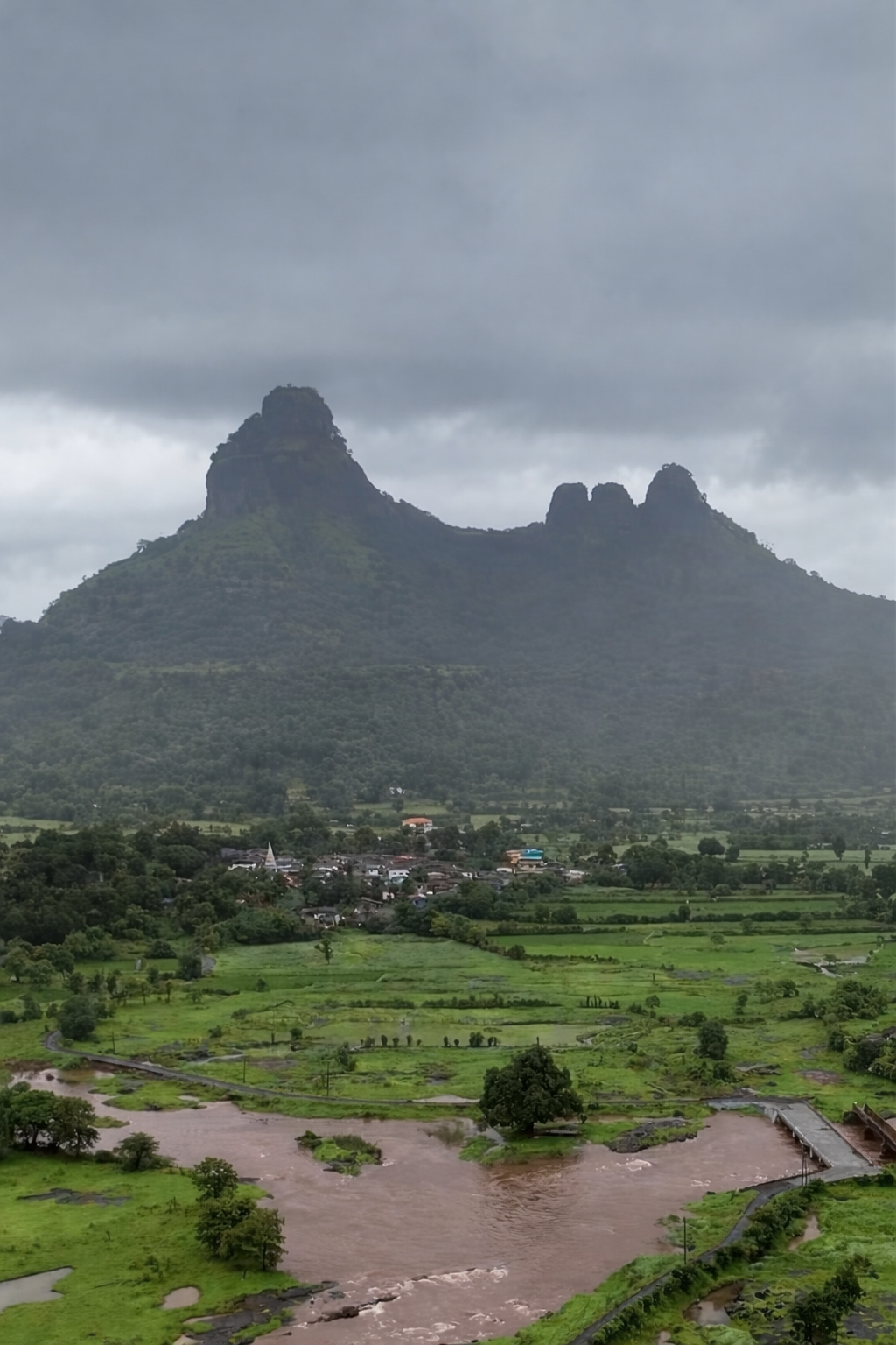 Scenic agricultural landscape by Growfarm with lush green fields, flowing river, and misty mountains under cloudy sky